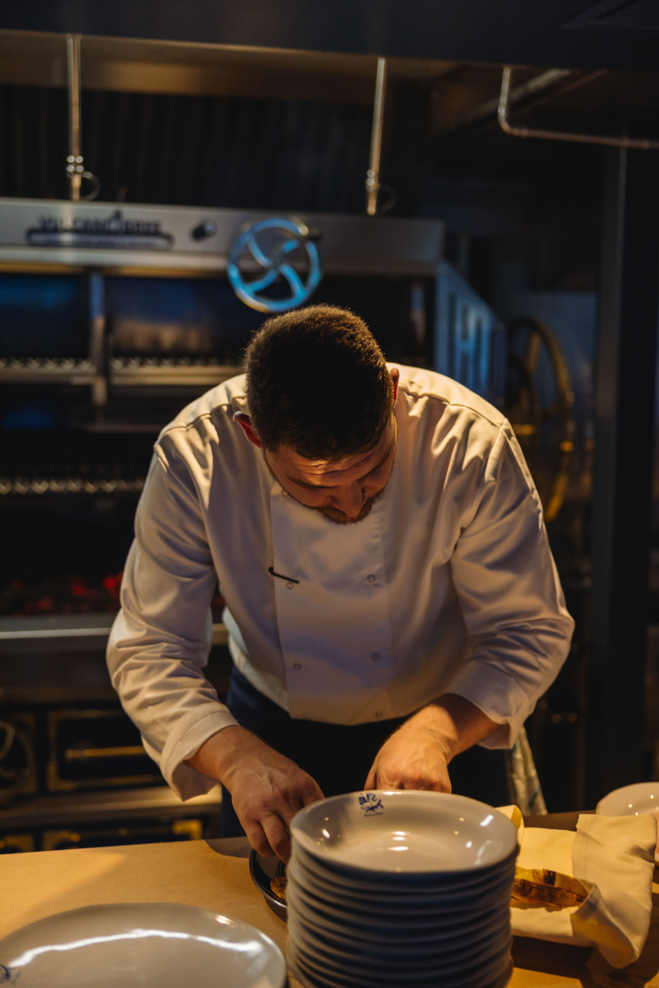 Beef&Bass chef plating at the pass in front of the charcoal grill